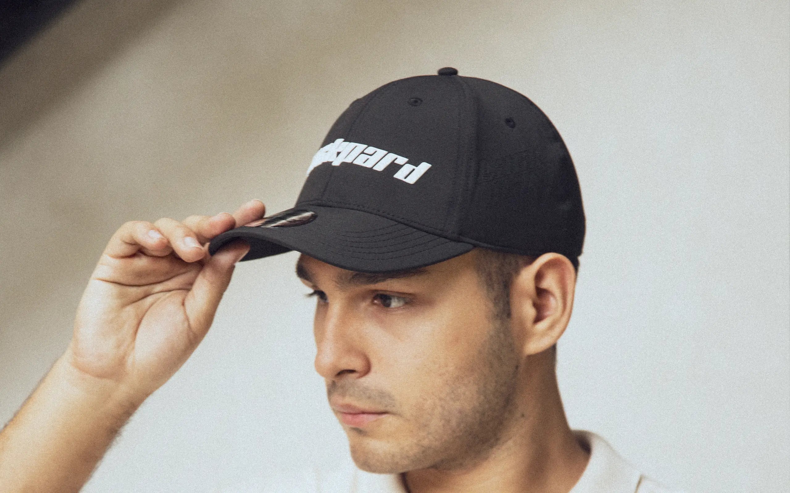 A man in a black Lackpard cap with a raised white wordmark, one hand on the visor.
