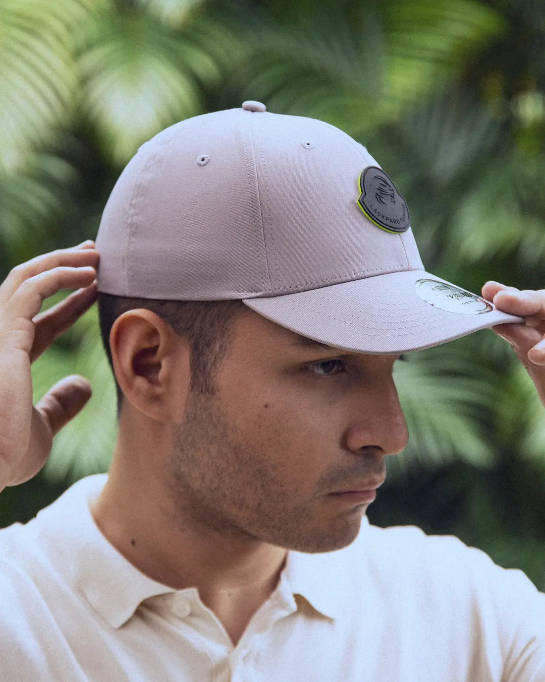 A man in profile in a taupe Lackpard cap with a round leopard patch, both hands on the cap.